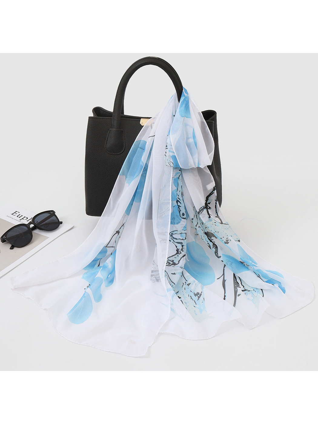 Light blue botanical print scarf draped over a black handbag