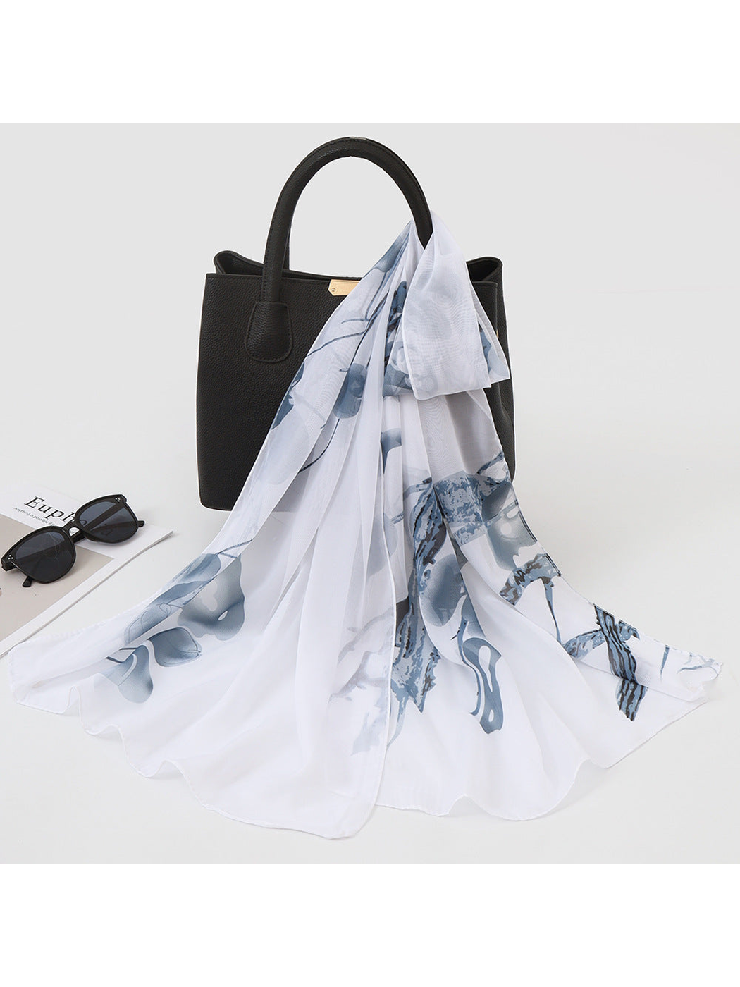 White scarf with gray botanical print draped over a black handbag