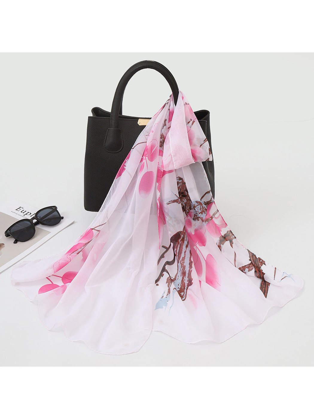 Light pink scarf with botanical print draped over a black handbag