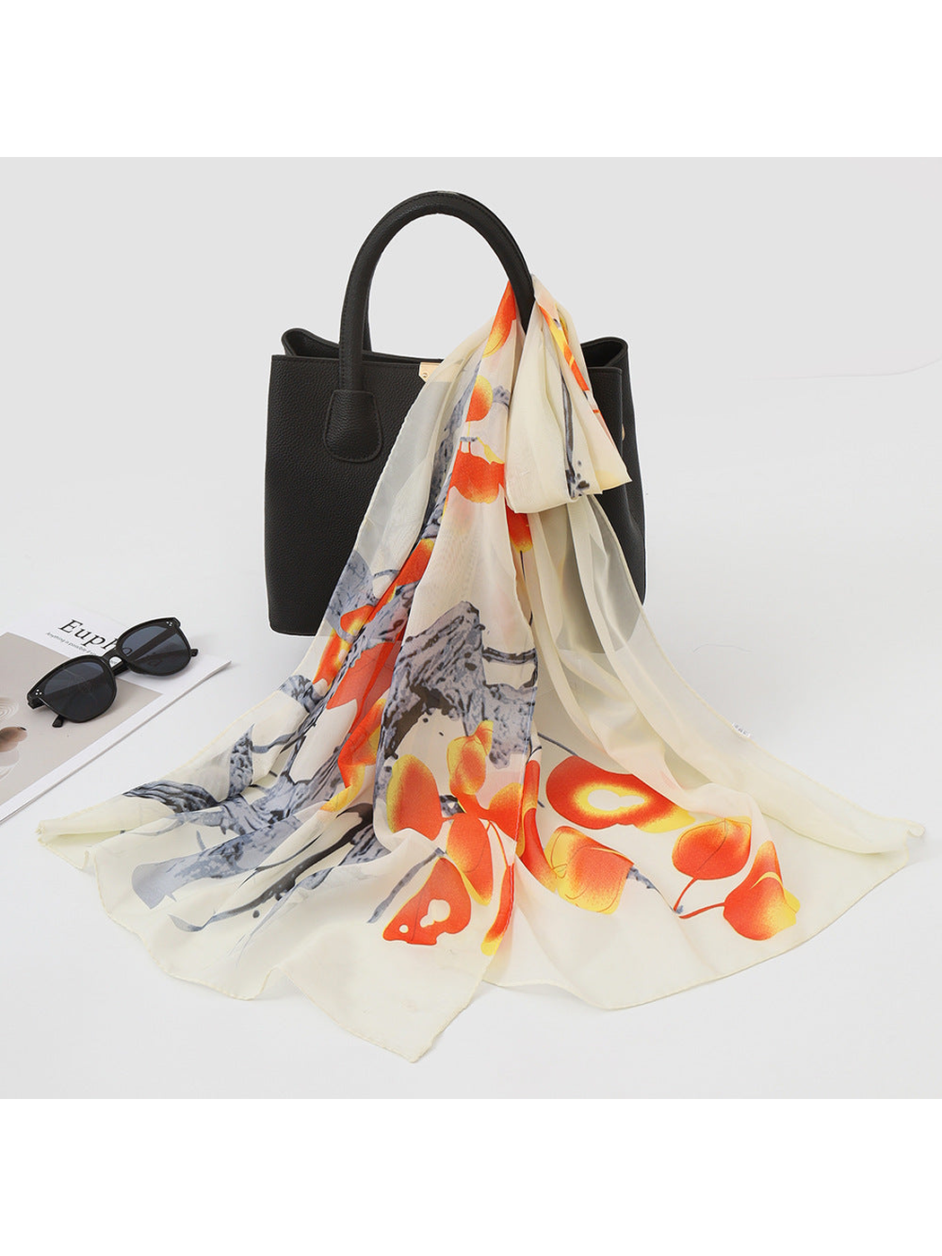 Cream scarf with orange botanical print draped over a black handbag