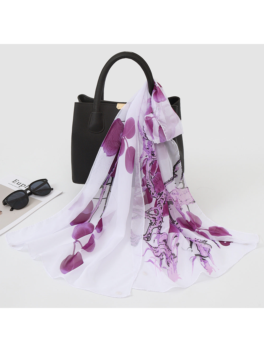 Purple scarf with abstract botanical print draped over a black handbag
