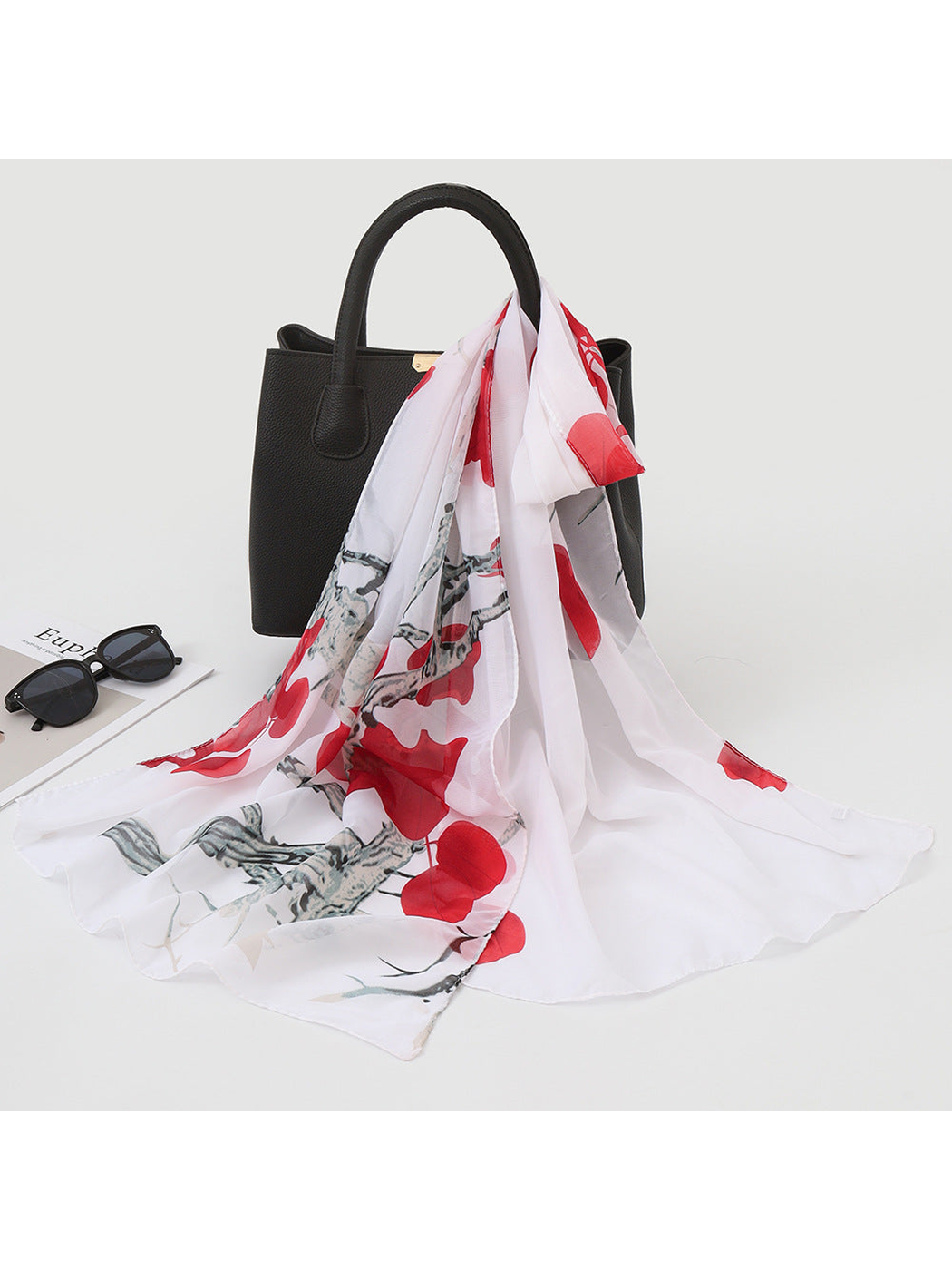 Red and white botanical print scarf draped over a black handbag