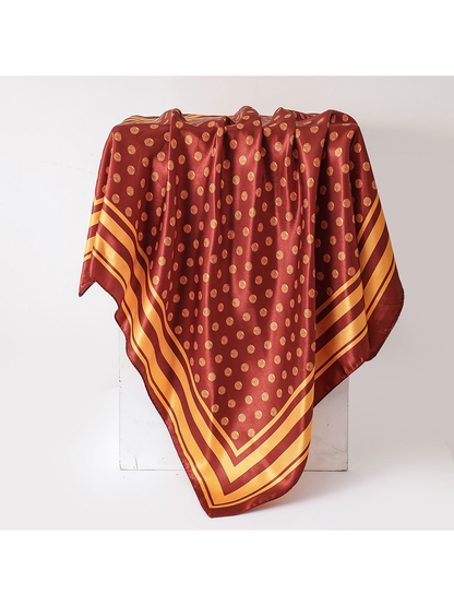 Orange-red square scarf with gold polka dots and striped border, draped view