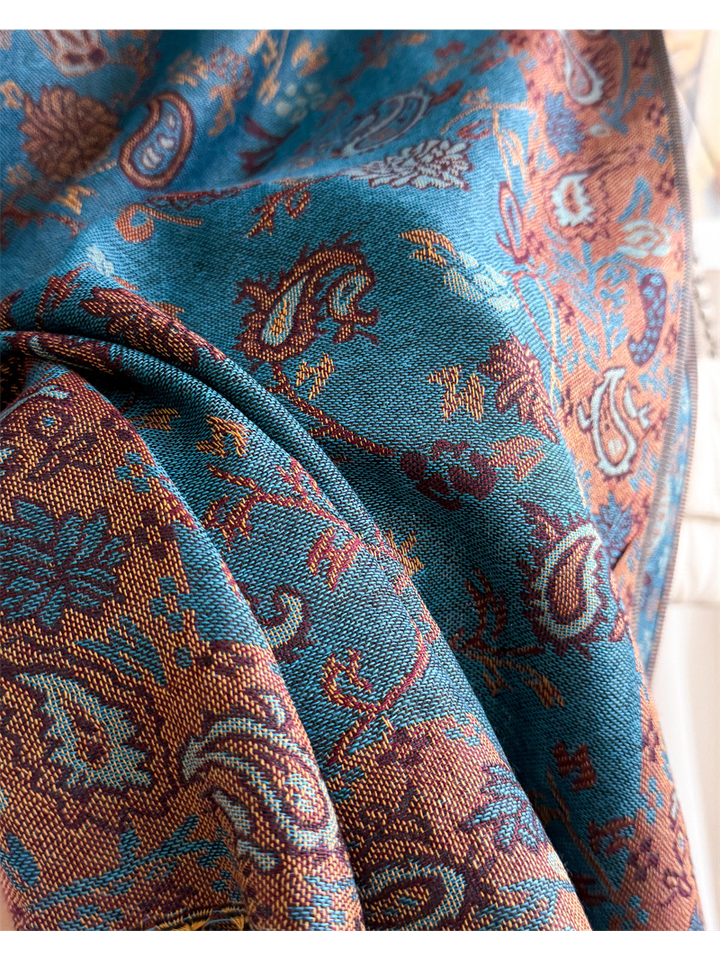 Macro view of the lake blue scarf's woven paisley pattern and ornamental border