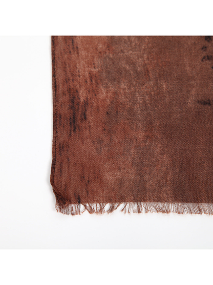 Close-up of the rust scarf's fine fringe and stitched side hem