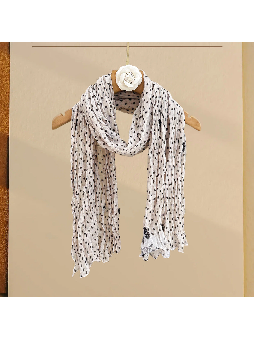 Ivory polka-dot scarf with wavy edges, draped on a hanger