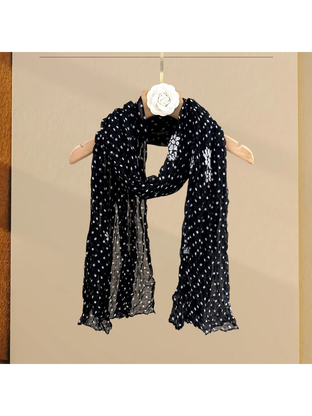 Black polka-dot scarf with floral accents, draped on a hanger