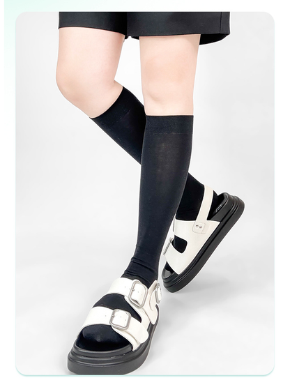 Black knee-high socks styled with white buckle sandals