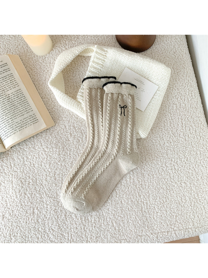 Beige cable-knit crew socks with black-edged cuffs and bow embroidery