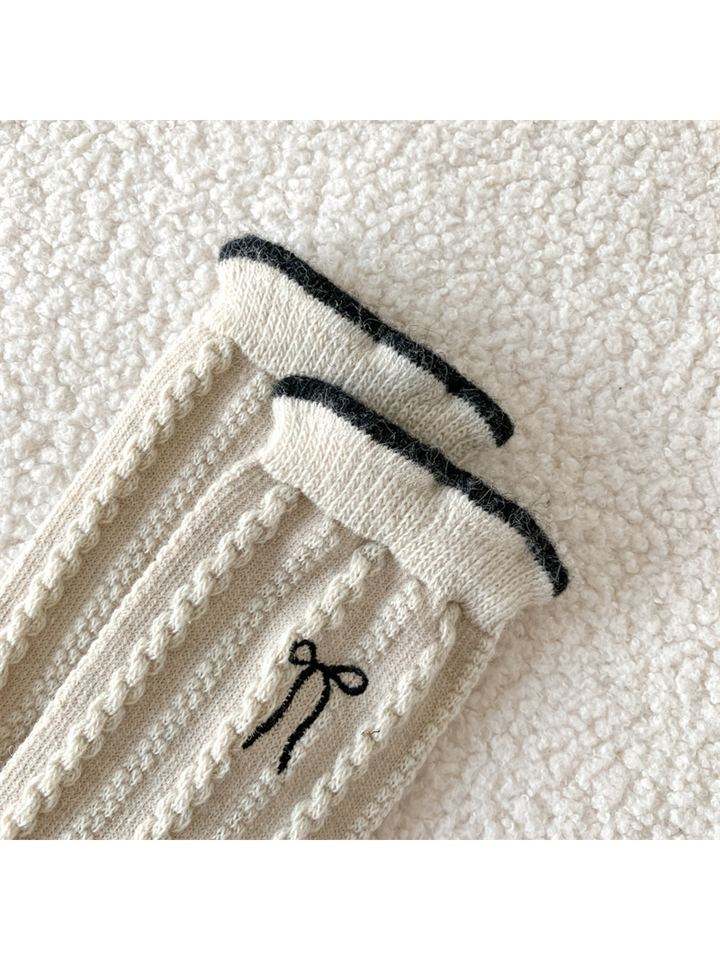Close-up of the contrast-edged cuff, cable-knit texture and bow embroidery
