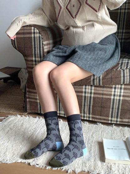 Gray tree-pattern crew socks worn in a seated indoor setting