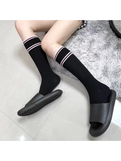 Black knee-high socks with pink stripes worn with black slide sandals
