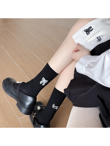 Black ribbed crew socks with bow and script embroidery worn with black shoes