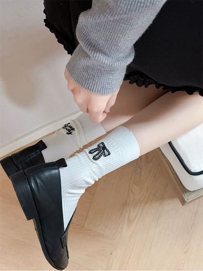 Ivory ribbed crew socks with bow and script embroidery worn with black loafers