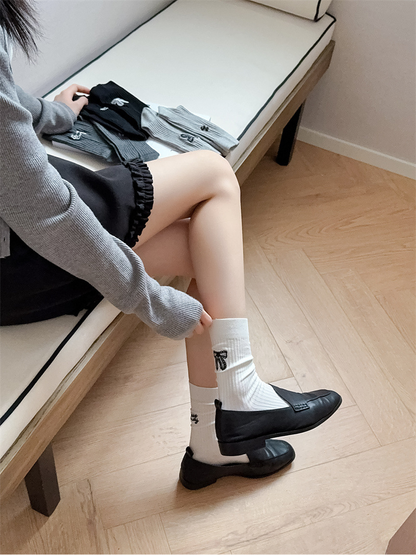 Ivory ribbed crew socks worn with black loafers in a seated view