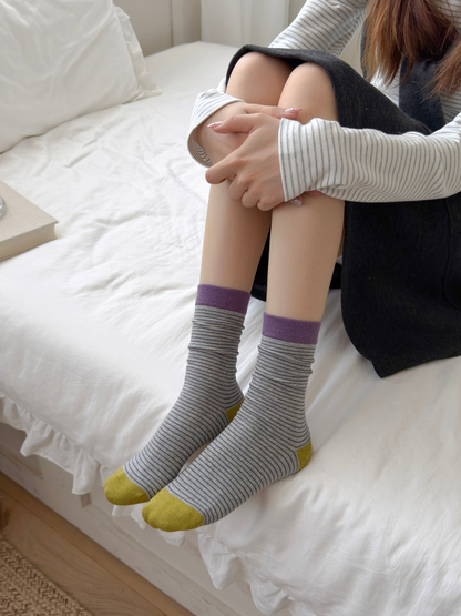 Gray striped crew socks with purple cuffs and green toes worn while seated