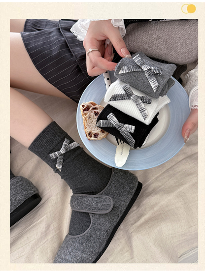 Dark gray plaid-bow crew socks worn with gray shoes beside folded color options