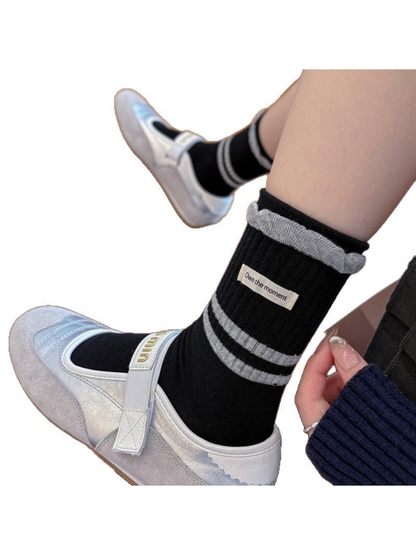 Close-up of the black sock's ribbed cuff, gray stripes, ruffled edge, and label