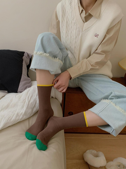 Brown ribbed crew socks with green toes and yellow cuff trim in a seated lifestyle view