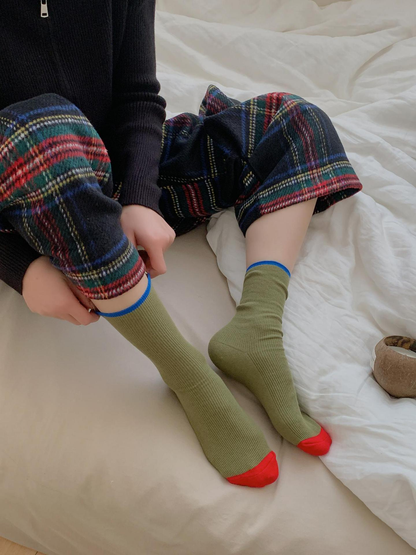 Green ribbed crew socks with red toes and blue cuff trim, worn pair