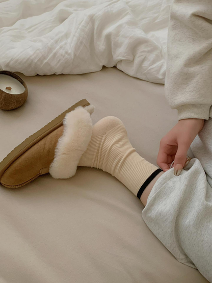 Close-up of a cream ribbed crew sock with black cuff trim worn with a lined slipper