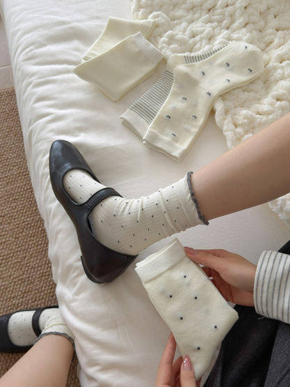 Ivory ruffled polka-dot crew socks worn with black flats beside folded styles