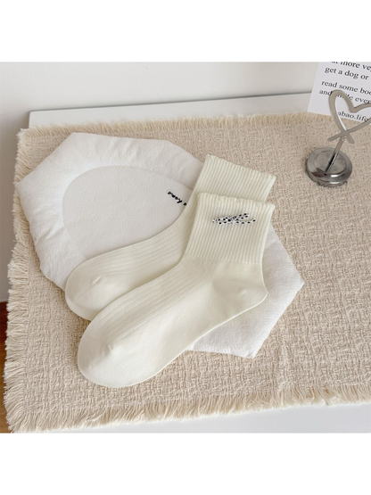 Ivory crew socks with a black and white bow at the cuff, laid flat