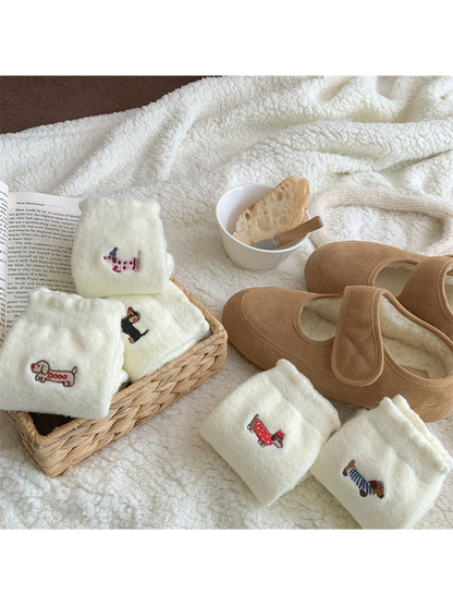 Folded ivory fuzzy dog motif socks arranged beside tan slippers