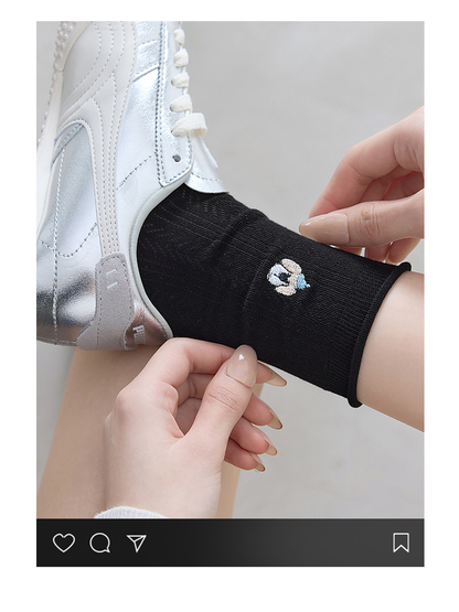 Close-up of a black crew sock with an embroidered blue-cap dog motif and rolled edge