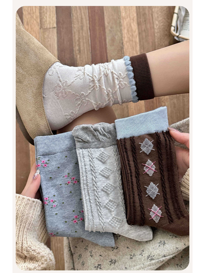 Ivory patterned crew socks worn with three additional sock styles held in hand