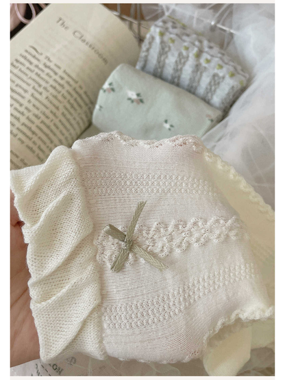 Close-up of an ivory sock with a gray bow, ruffled cuff and openwork panels