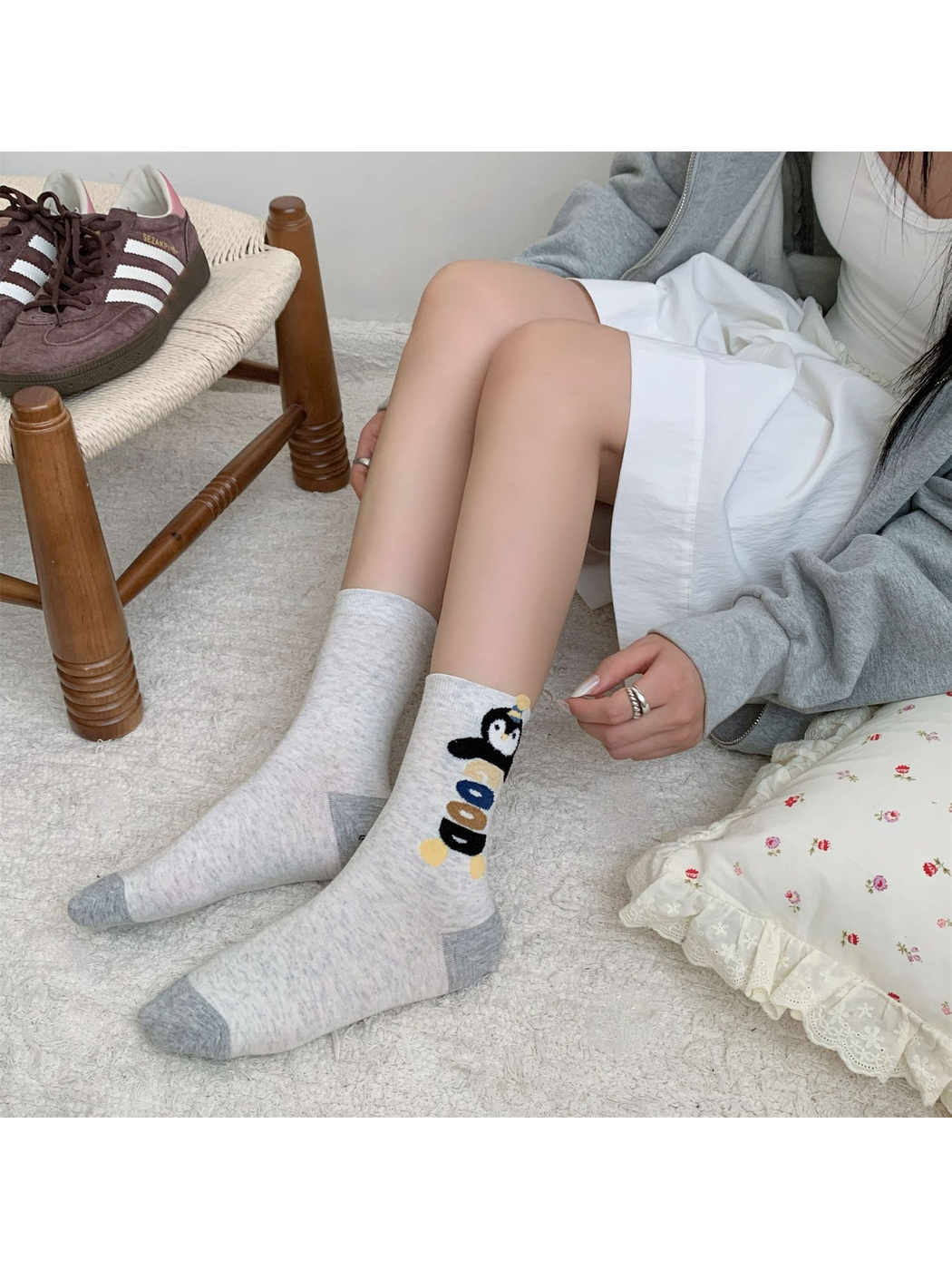 Greige stacked penguin crew socks worn in a seated setting