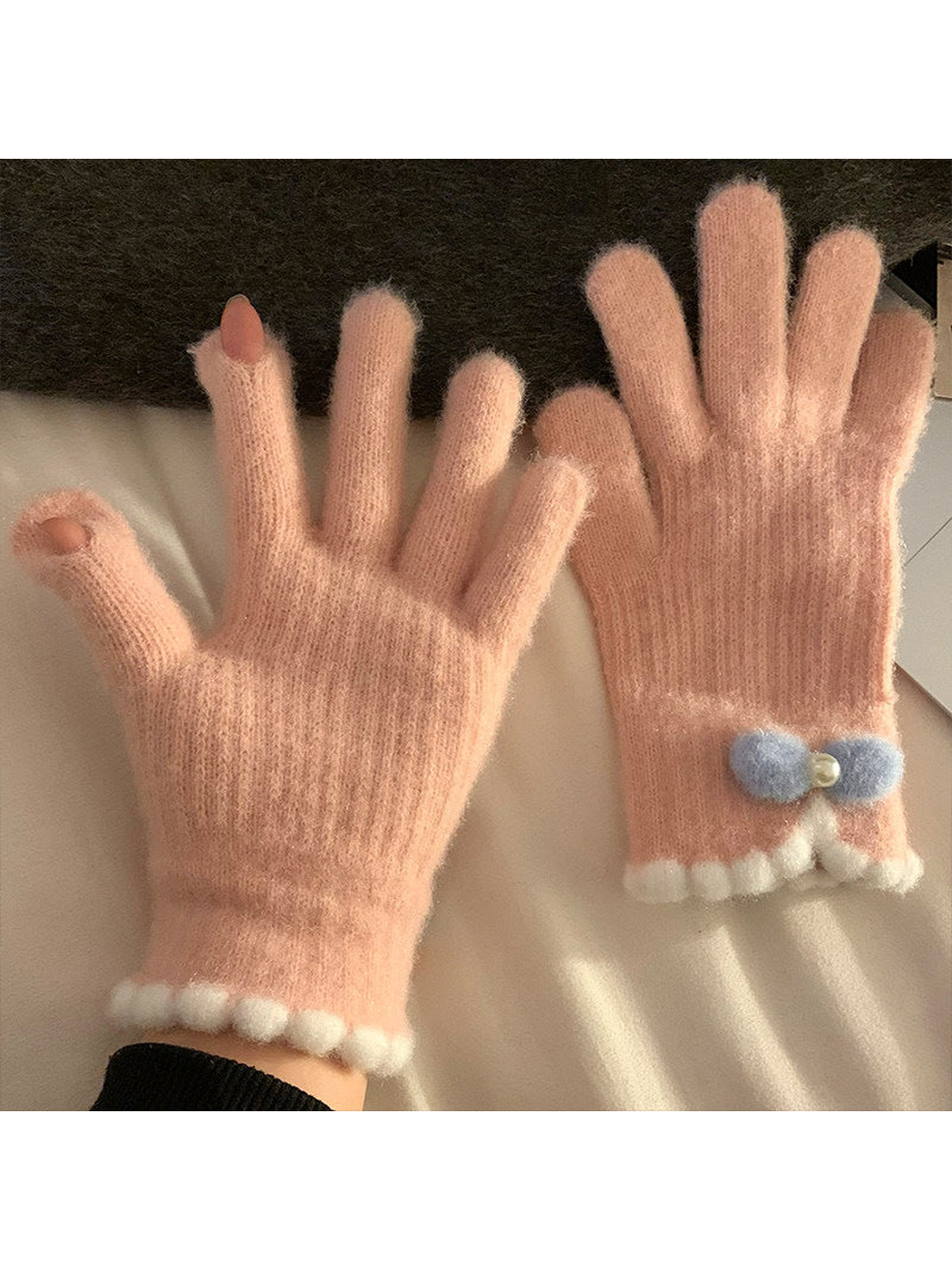 Light pink fuzzy gloves with open fingertips and blue bow-accent cuff
