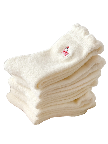 Stack of ivory fuzzy crew socks with ruffled cuffs and dog embroidery