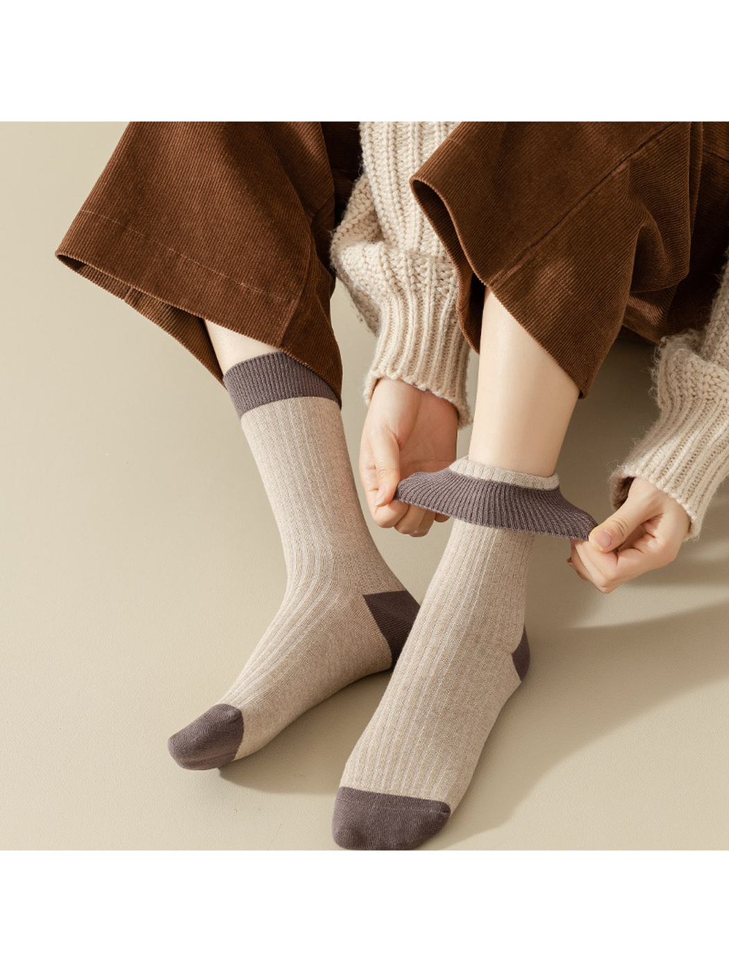 Beige ribbed crew socks with contrasting cuffs being stretched