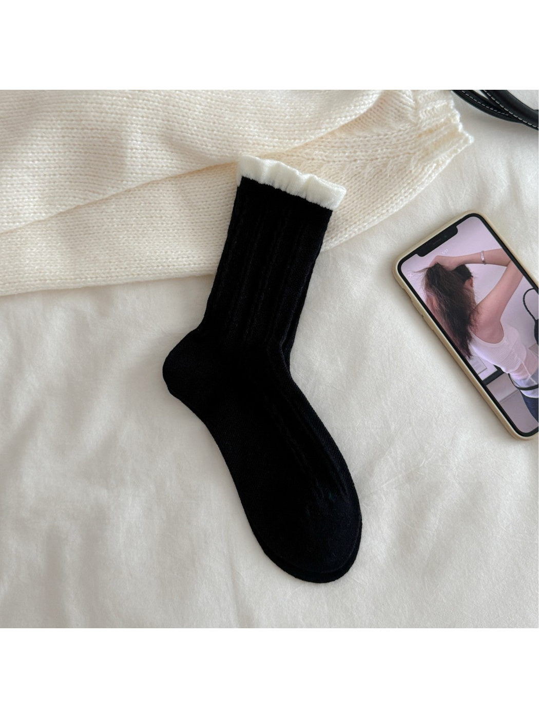 Black cable-knit crew sock with contrasting white ruffled cuff, flat view