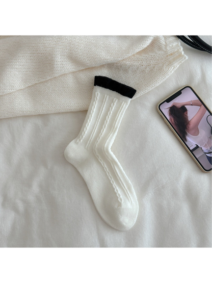 White cable-knit crew sock with contrasting black ruffled cuff, flat view