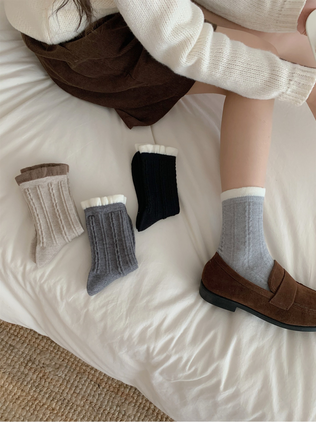 Light gray cable-knit crew socks styled with brown loafers beside three additional colors
