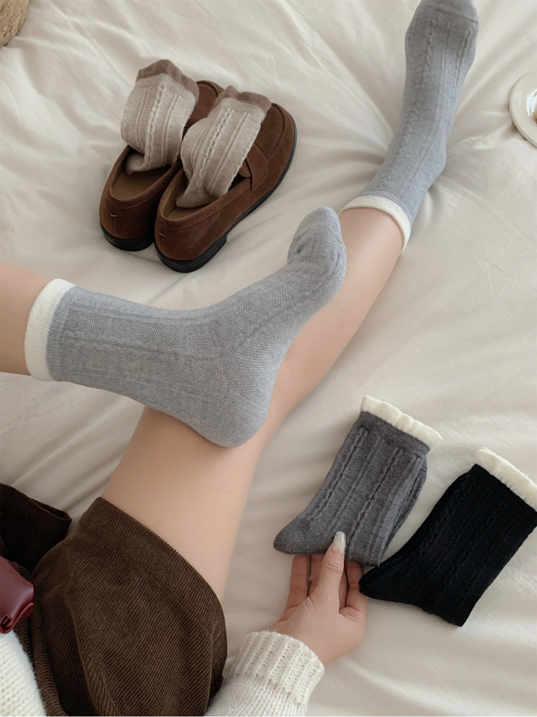 Light gray cable-knit crew socks worn with contrasting white cuffs beside brown loafers and additional colors