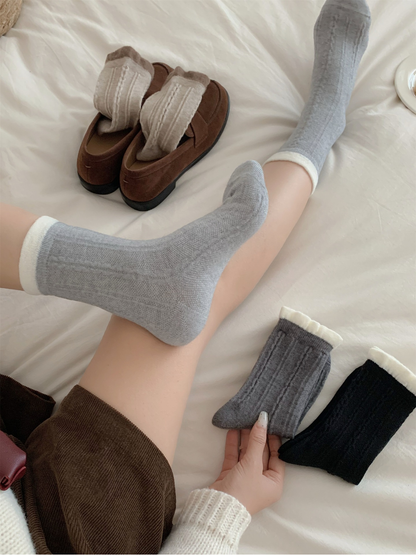 Light gray cable-knit crew socks worn with contrasting white cuffs beside brown loafers and additional colors
