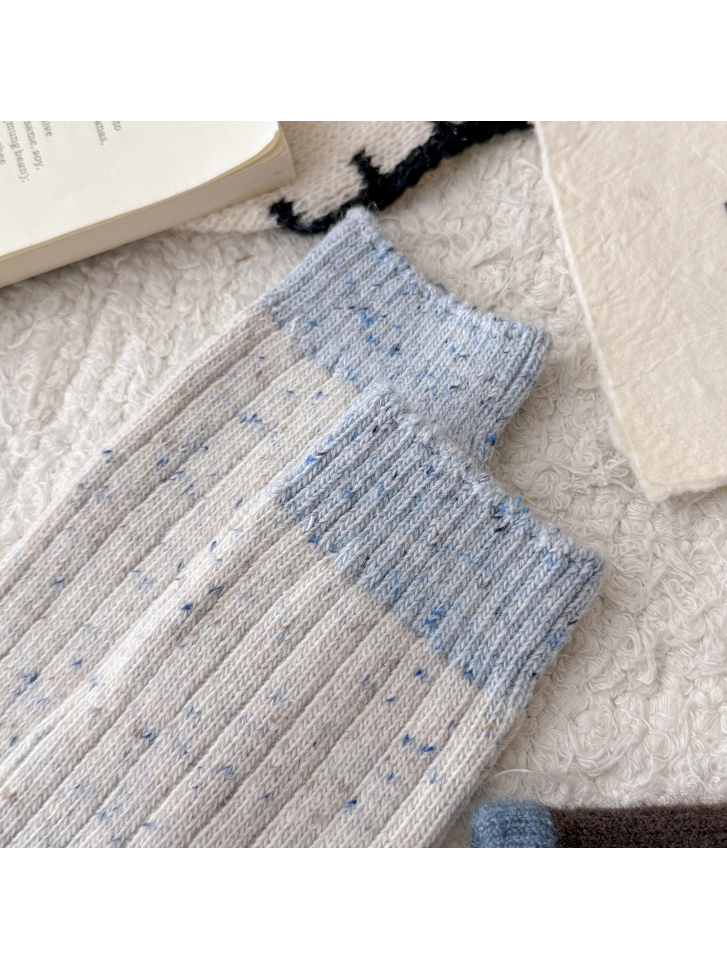 Close-up of the light blue ribbed cuff and cream speckled knit