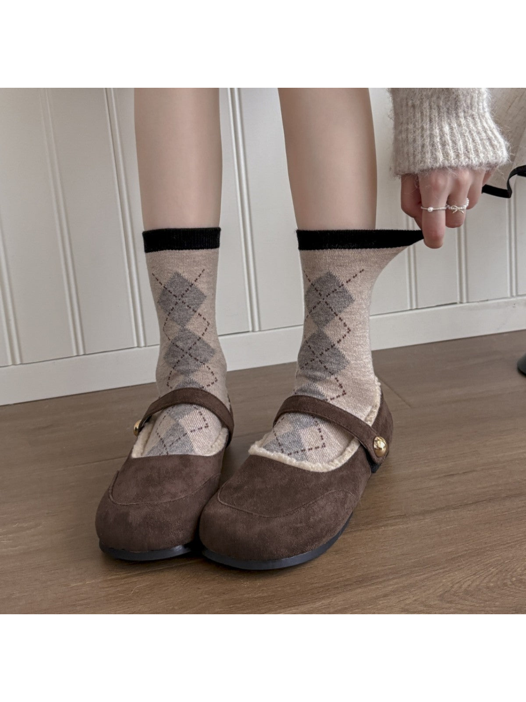 Beige argyle crew socks worn with brown shoes while the cuff is gently stretched