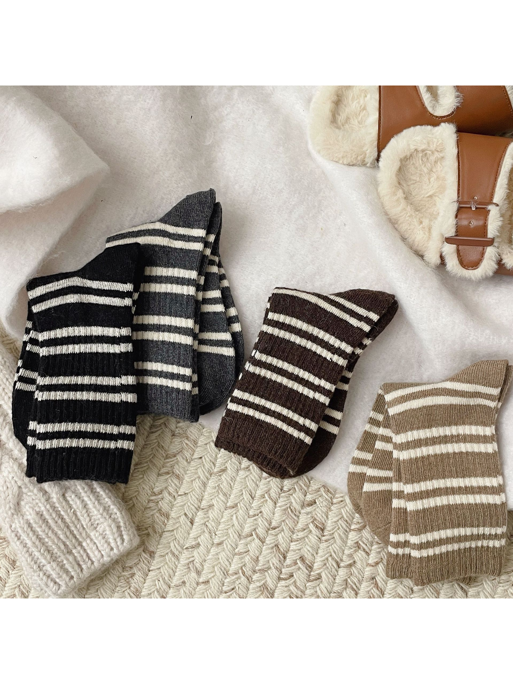 Black, gray, brown and khaki striped crew socks arranged on a textured cream surface