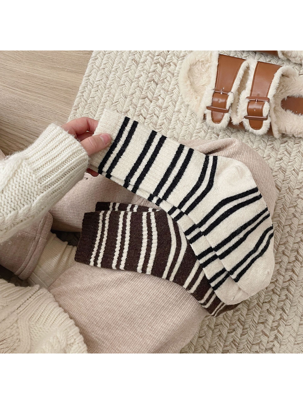 Ivory and dark brown striped crew socks held across a seated model's lap