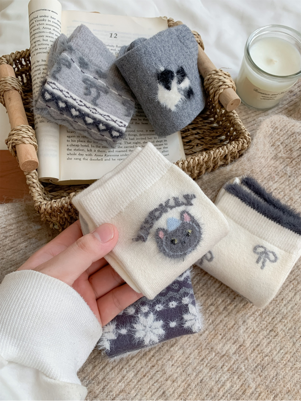 Hand holding an ivory crew sock with a fuzzy cat-face motif