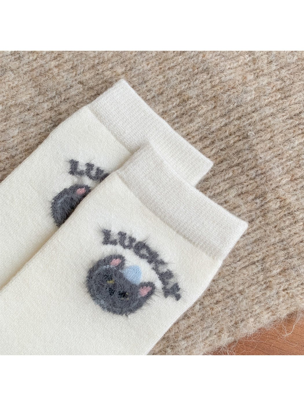 Close-up of fuzzy cat-face motifs below ribbed ivory cuffs