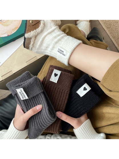 Cream socks worn with lined brown clogs beside folded gray, brown and black color options