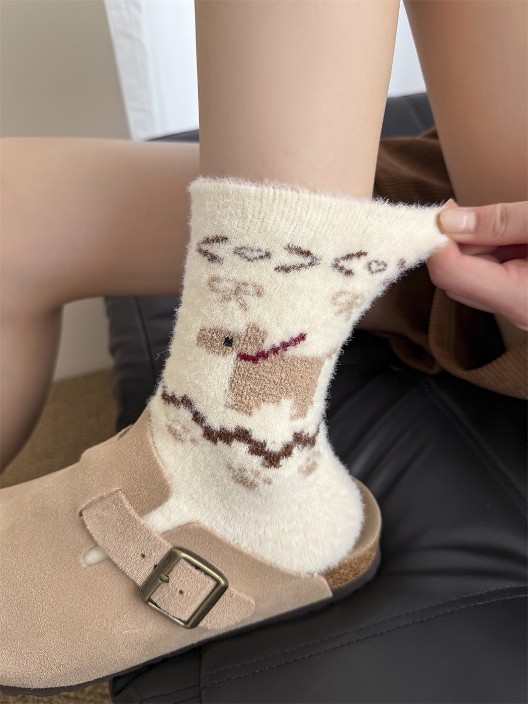Close view of an ivory dog-motif fuzzy sock with its ribbed cuff gently pulled