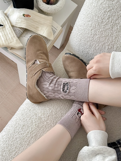 Light taupe cable-knit crew socks worn with tan clogs in a seated view