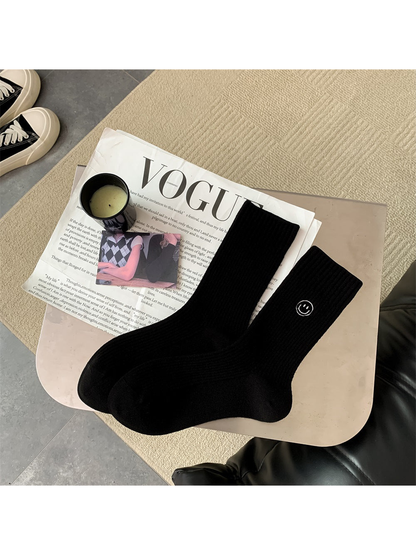 Black ribbed crew socks with embroidered smiley motif, pair laid flat